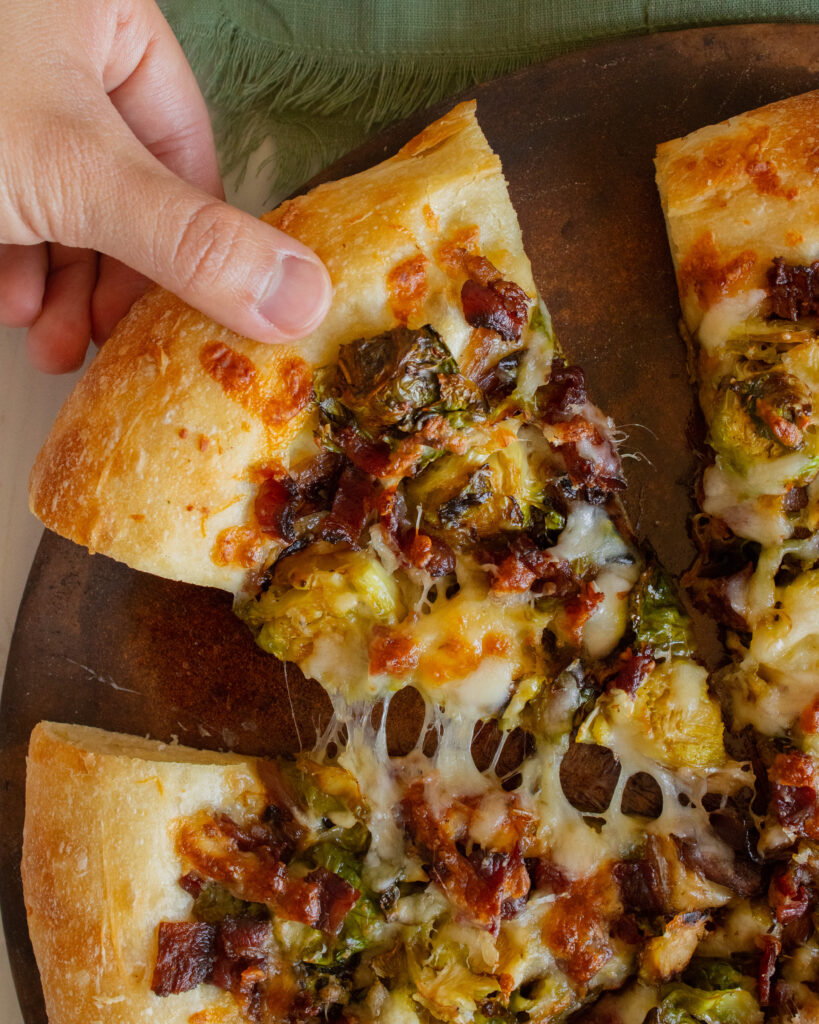 overhead shot of cheese pull slice of Brussels Sprouts & Bacon Pizza