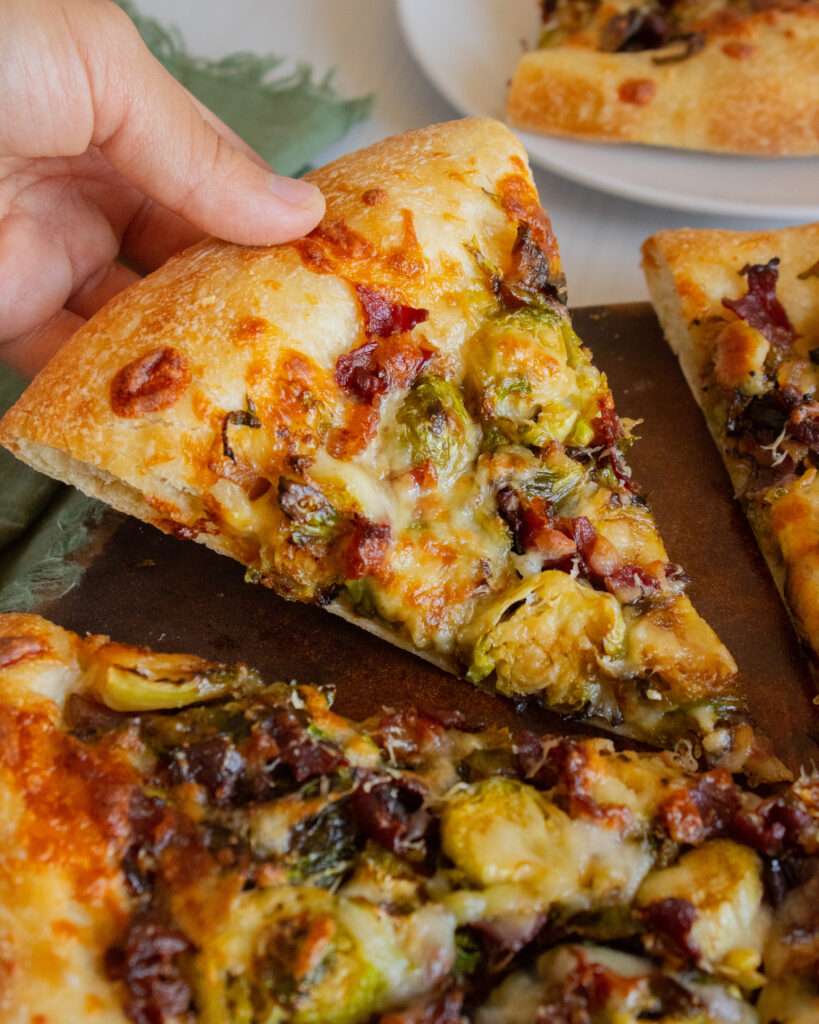 holding a slice of Brussels Sprouts & Bacon Pizza