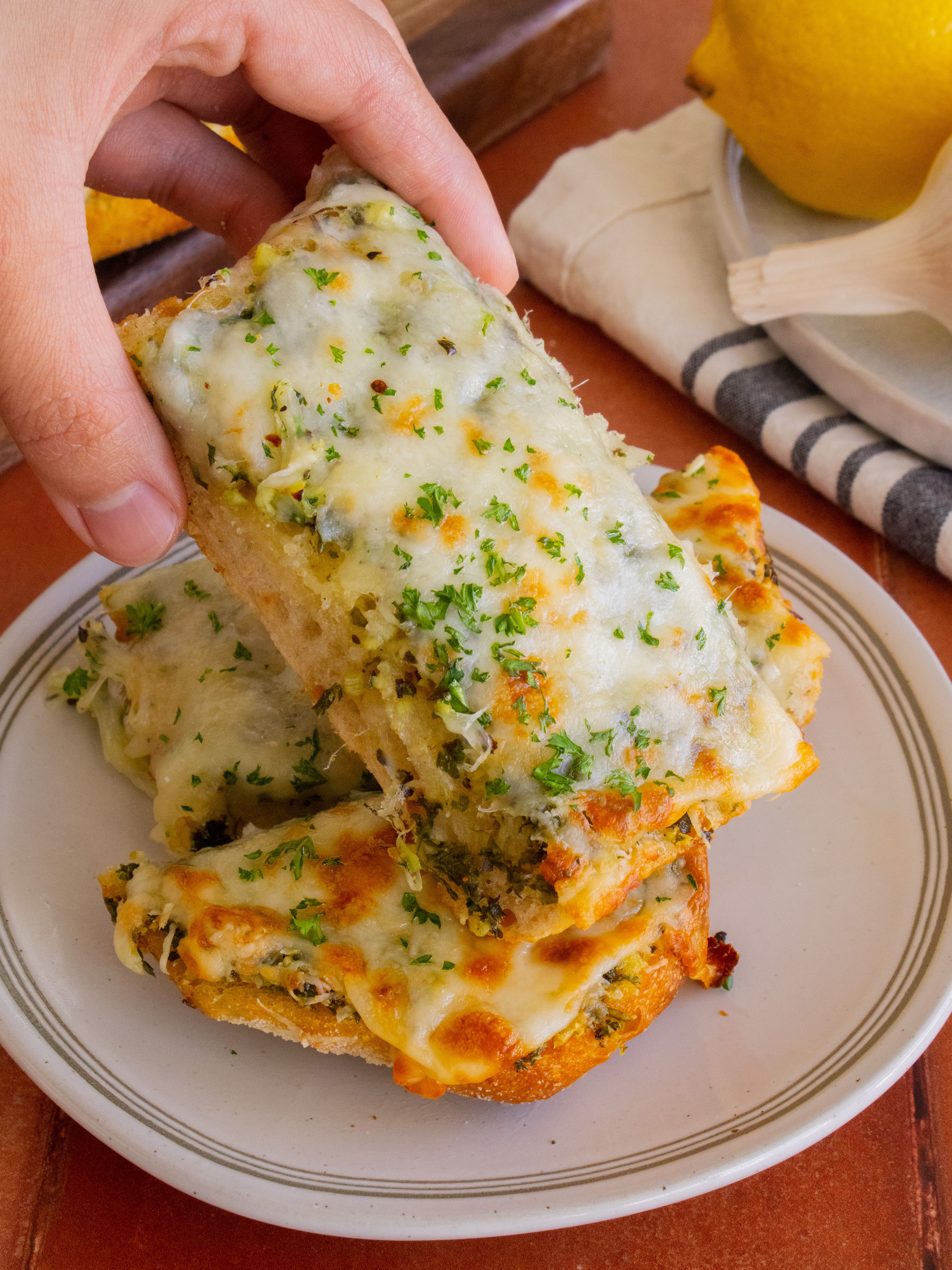 hand picking up a slice of Cheesy Garlic Bread from a plate