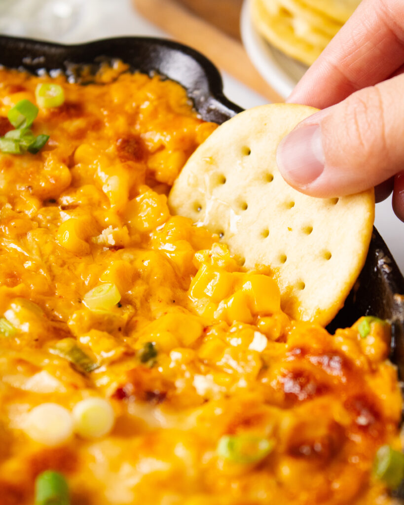 close up of crackers dipping into kimchi corn cheese dip
