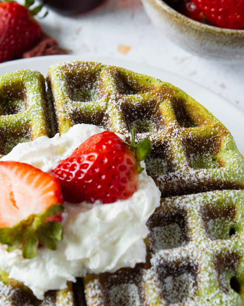 Close up of strawberry and whipped cream topping on matcha mochi waffles