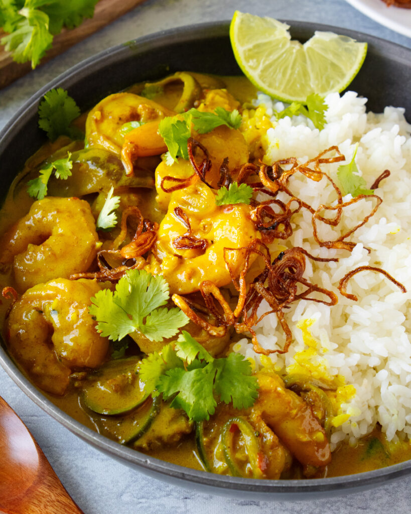 Bowl of Creamy Turmeric Shrimp Curry served with rice, crispy shallots, cilantro, and a lime wedge