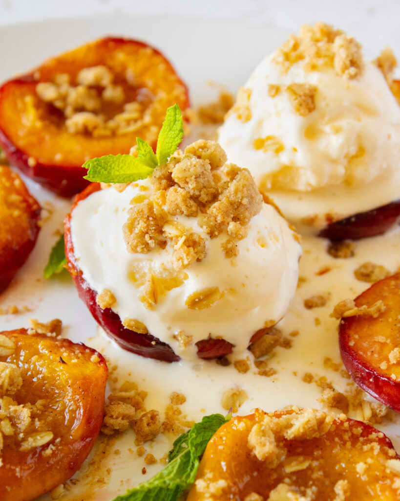 close up of roasted peach crisp with vanilla ice cream melting on top