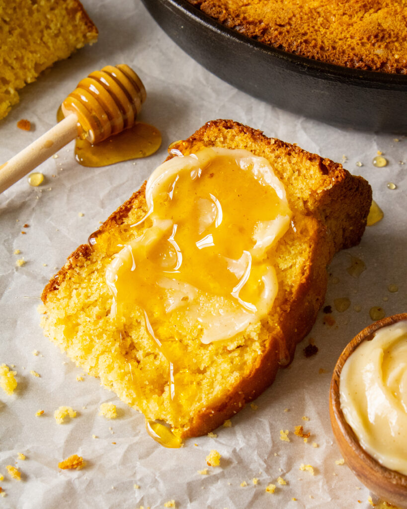 slice of Honey Butter Cornbread laying down on its side with honey butter and honey on top