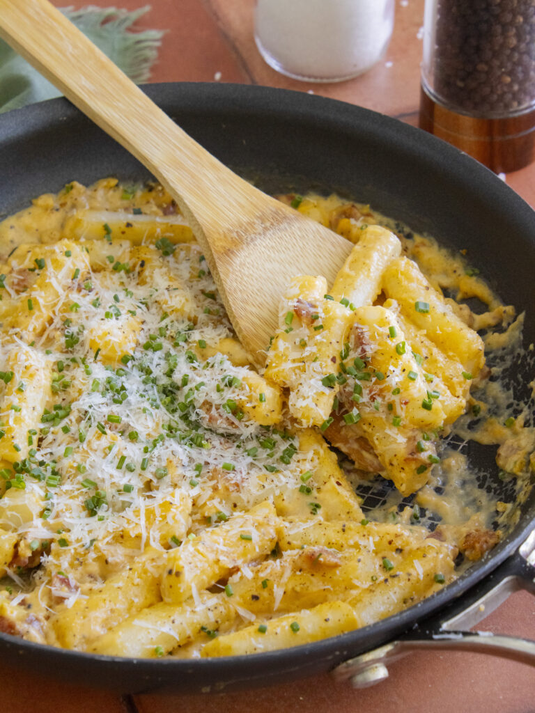 Carbonara Tteokbokki scooped onto a spoon resting in the pan
