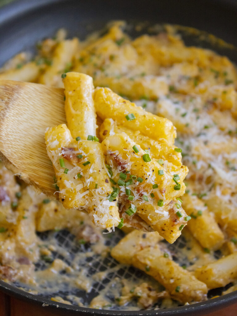 Carbonara Tteokbokki scooped onto a wooden spoon