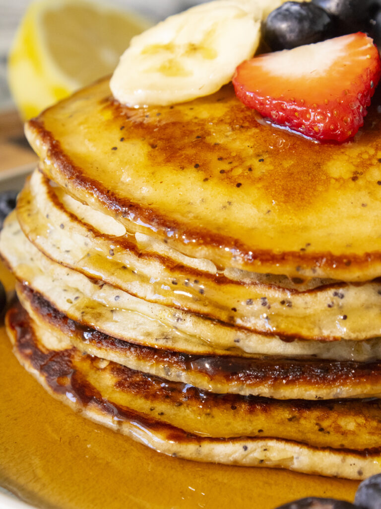 close up of a stack of Lemon Poppyseed Pancakes with maple syrup dripping down the sides