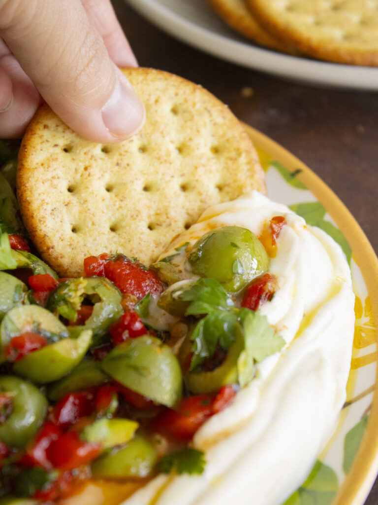 close up of scooping Whipped Ricotta & Olive Dip with a cracker